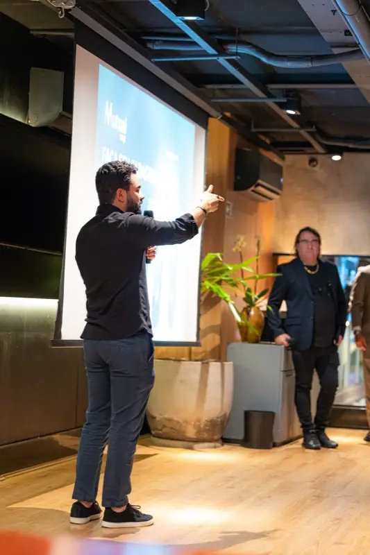 Palestrante no palco aponta para o telão enquanto fala ao público.