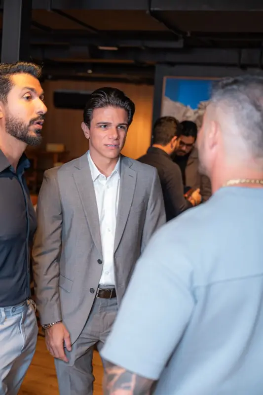 Participantes conversam em pé no salão, em pequeno grupo.