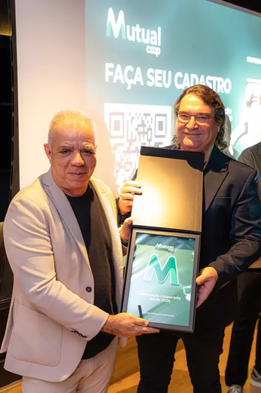 Entrega de placa de reconhecimento da Mutualcoop a um participante, diante do telão.