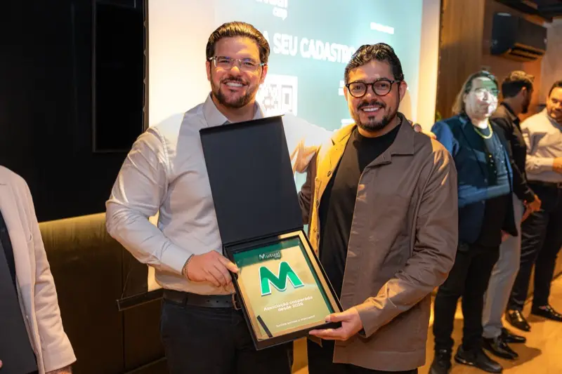 Dois participantes seguram a placa de reconhecimento da Mutualcoop entregue no encontro.